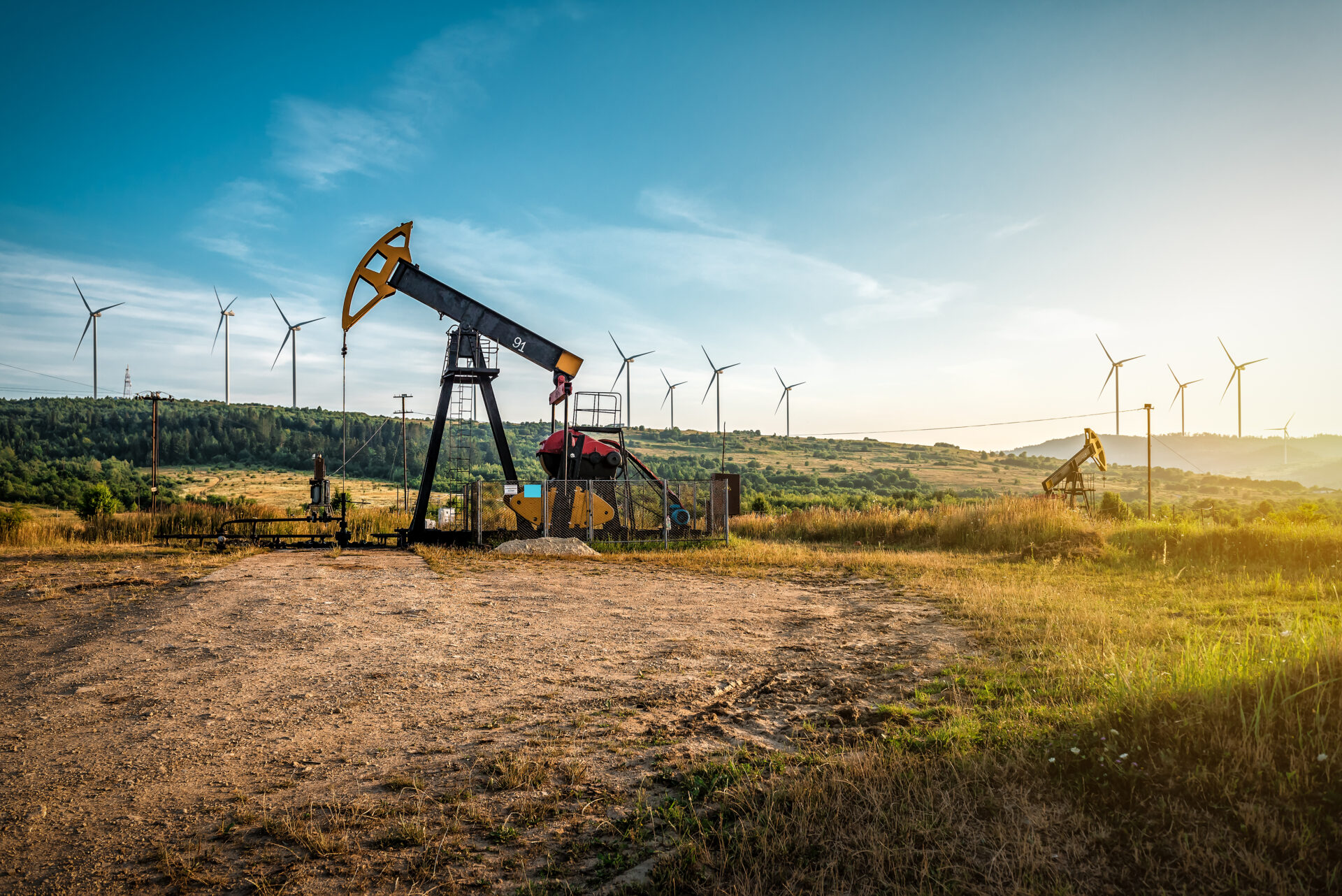 Oil pump and wind turbines against incredible sunset sky. Industrial concept